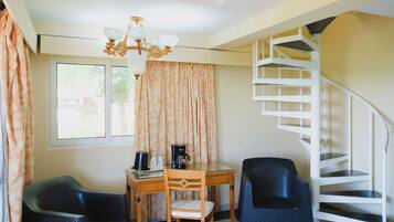 A room with a spiral staircase, a wooden desk with a chair, a black chair, and a window with curtains.