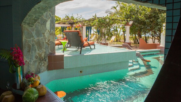 A swimming pool area with tiled flooring, a stone archway, and lounge chairs. - Las Olas Resort (Guarumal)