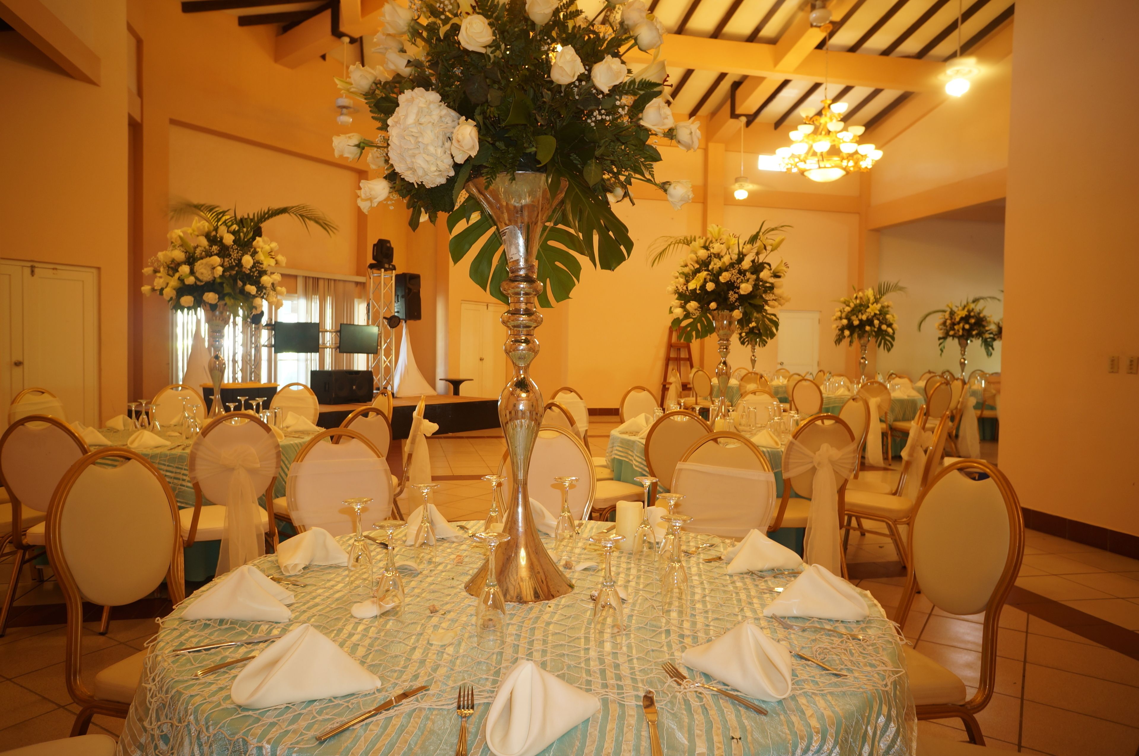Un salón de banquetes con mesas redondas dispuestas para el servicio de comidas, cada una con un centro de mesa floral y manteles blancos.