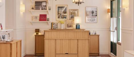 A hotel lobby with a wooden reception desk, pendant lighting, and framed photographs on the walls.