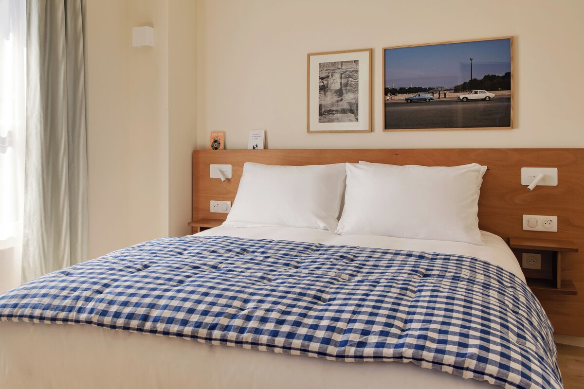 A neatly made bed with a checkered bedspread, two pillows, and a headboard with a wooden finish.