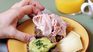 A plate with a slice of bread topped with avocado, cheese, and meat.