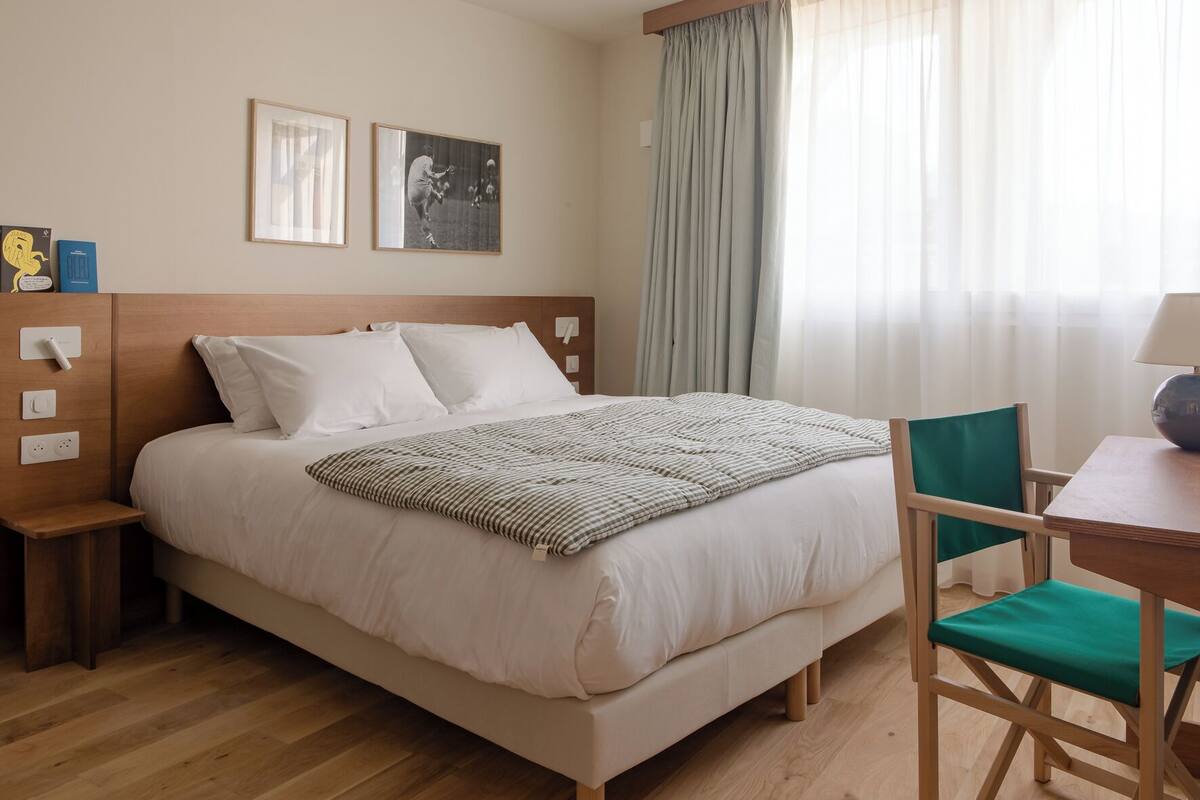 Une chambre d’hôtel comprenant un lit, une table de chevet, une chaise et un bureau avec une lampe.