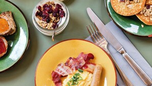 Ein Frühstückstisch mit Toast, Rührei, Speck, Pfannkuchen und einer Tasse Kaffee.