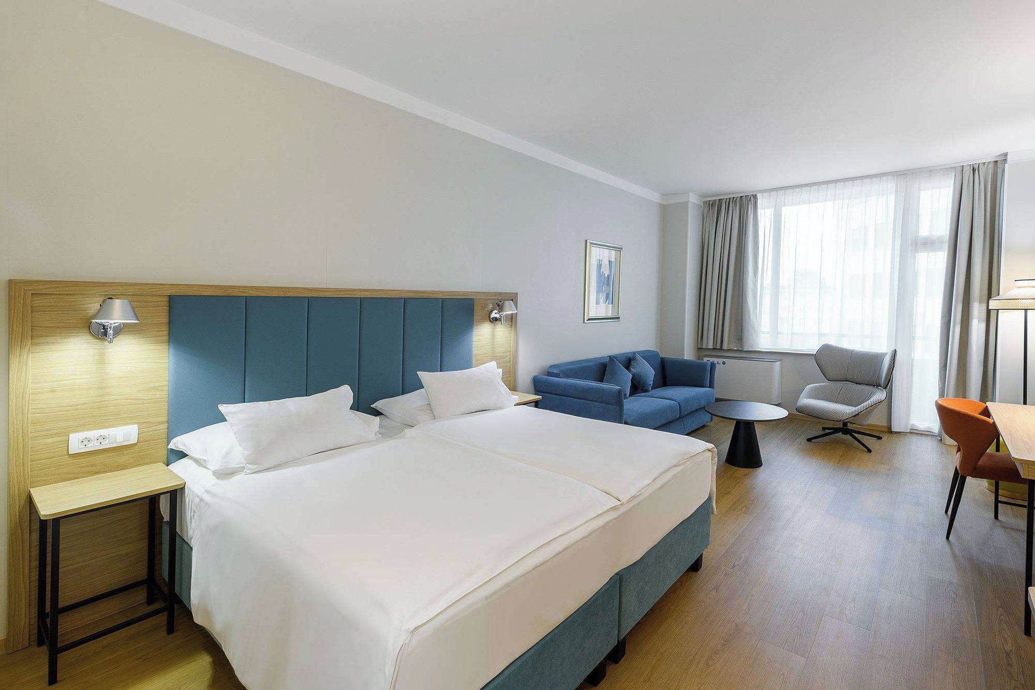 A hotel room with a large bed, a sofa, a small table, and a chair.