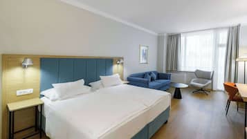 A hotel room with a large bed, a sofa, a small table, and a chair.