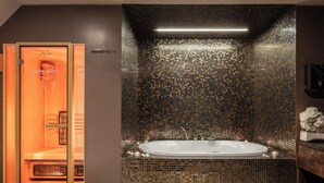Un cuarto de spa con una bañera grande y ovalada, una sauna de madera y una pared de azulejos con un diseño de mosaico.