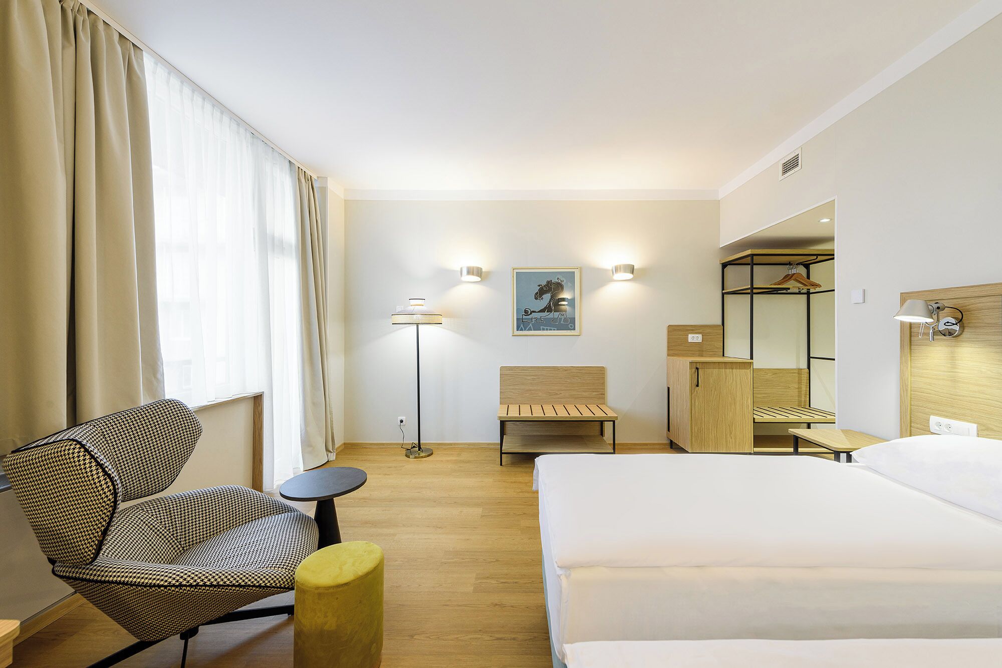 Een hotelkamer met een bed, een stoel, een bureau, een lamp en een schilderij aan de muur.