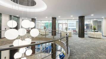 A modern hotel lobby with a central staircase, round tables, and a glass railing.