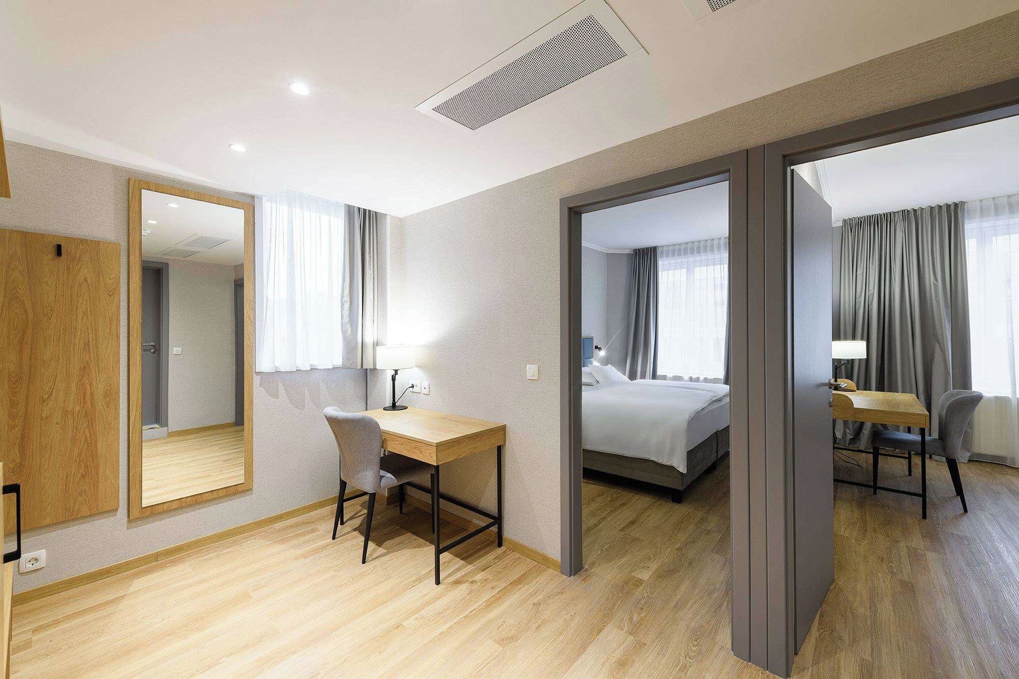A hotel room with a wooden desk, a bed, and a large mirror.
