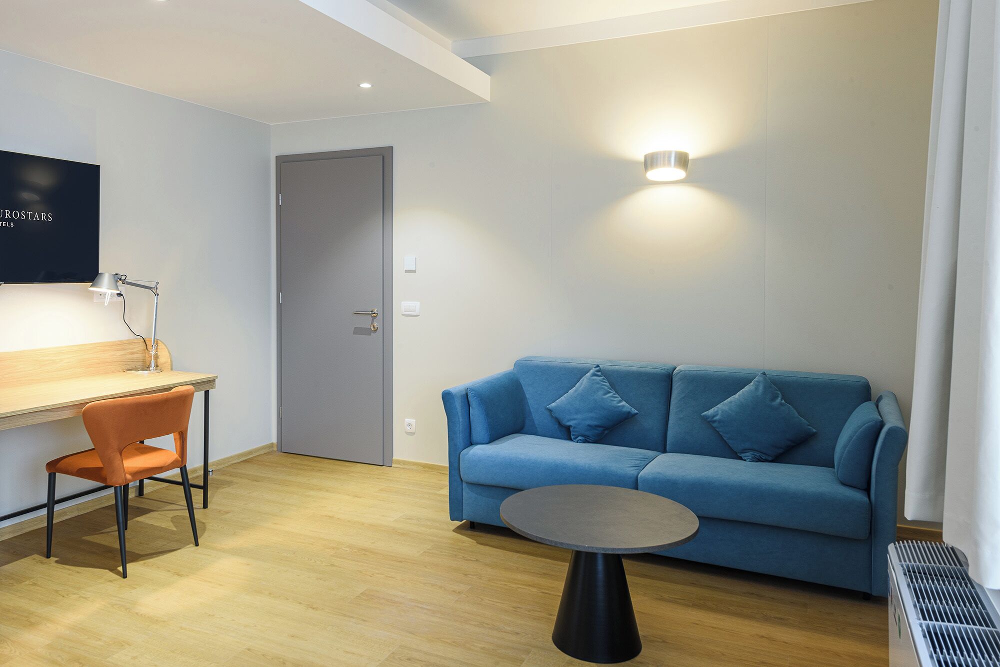 A modern room with a blue sofa, a round table, a wooden desk, and a chair.