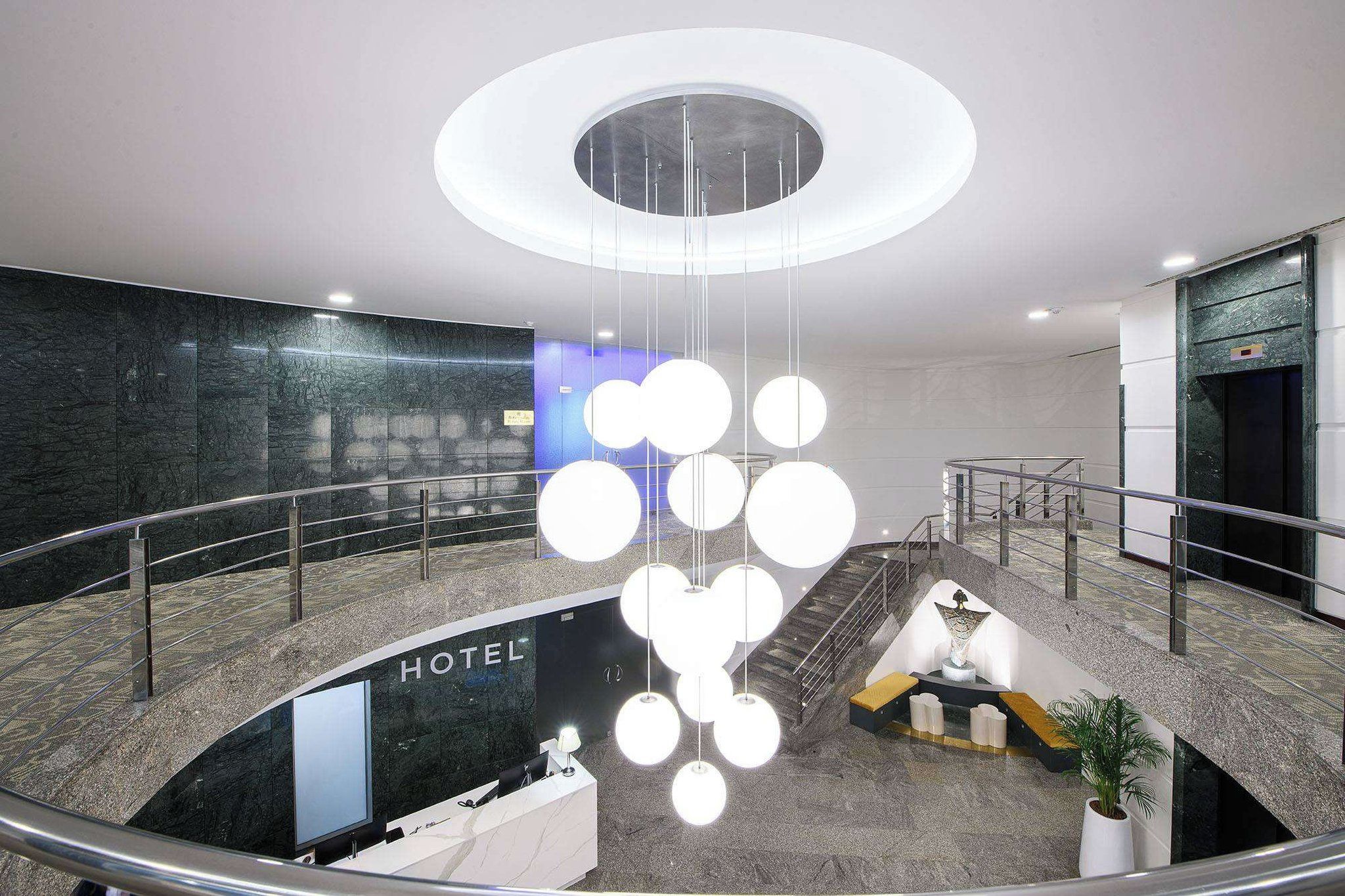 En hotellobby med modern design, med en central, cirkelformad lampa, en trappa och en receptionsdisk.