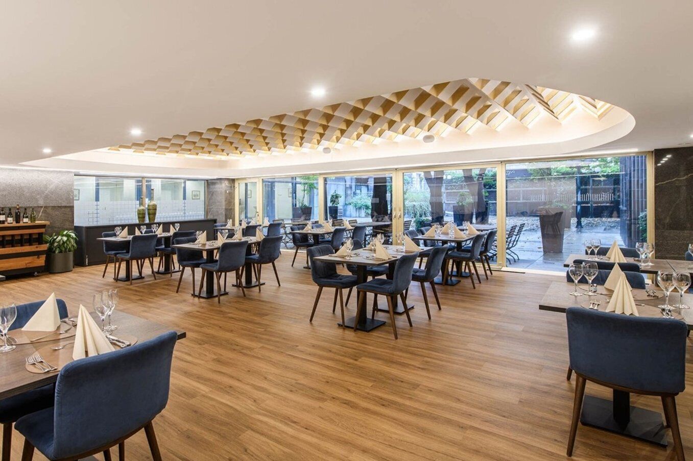 Een modern restaurant met houten vloeren, donkerblauwe stoelen en gedekte tafels.