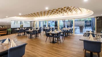 Een modern restaurant met houten vloeren, donkerblauwe stoelen en gedekte tafels.