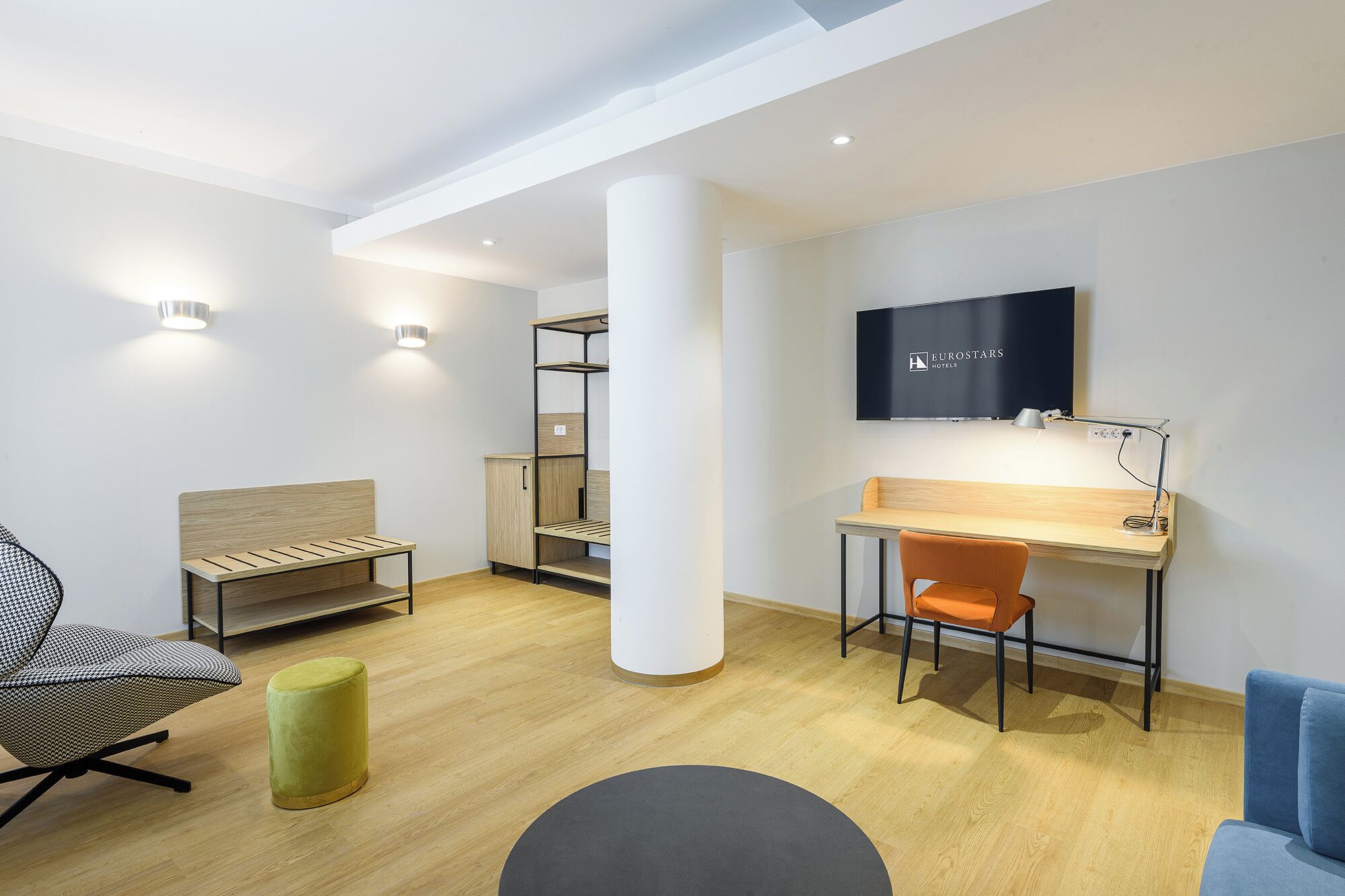 A modern hotel room with a desk, chair, and a television mounted on the wall.