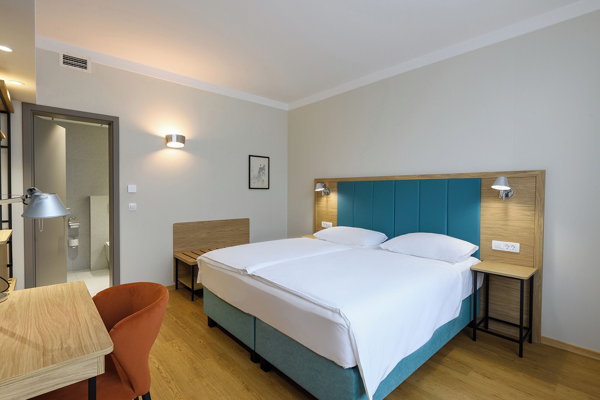 Hotellihuone, jossa on sänky, työpöytä, tuoli ja kaksi yöpöytää, joissa on lamput.
