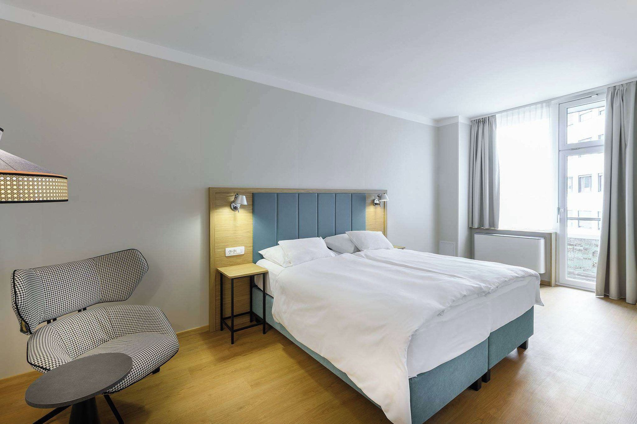 A hotel room with a bed, a chair, a nightstand, and a window with curtains.