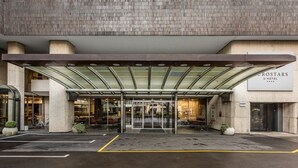 La entrada del Hotel Grostars U, con un acceso cubierto, puertas de vidrio y un estacionamiento al frente.