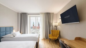 Habitación de hotel con dos camas, un escritorio, una silla, un televisor y vistas a un paisaje urbano.