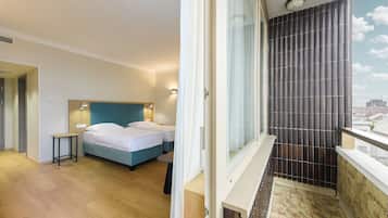 Habitación de hotel con cama, mesita de noche y vistas a la ciudad a través de una ventana.