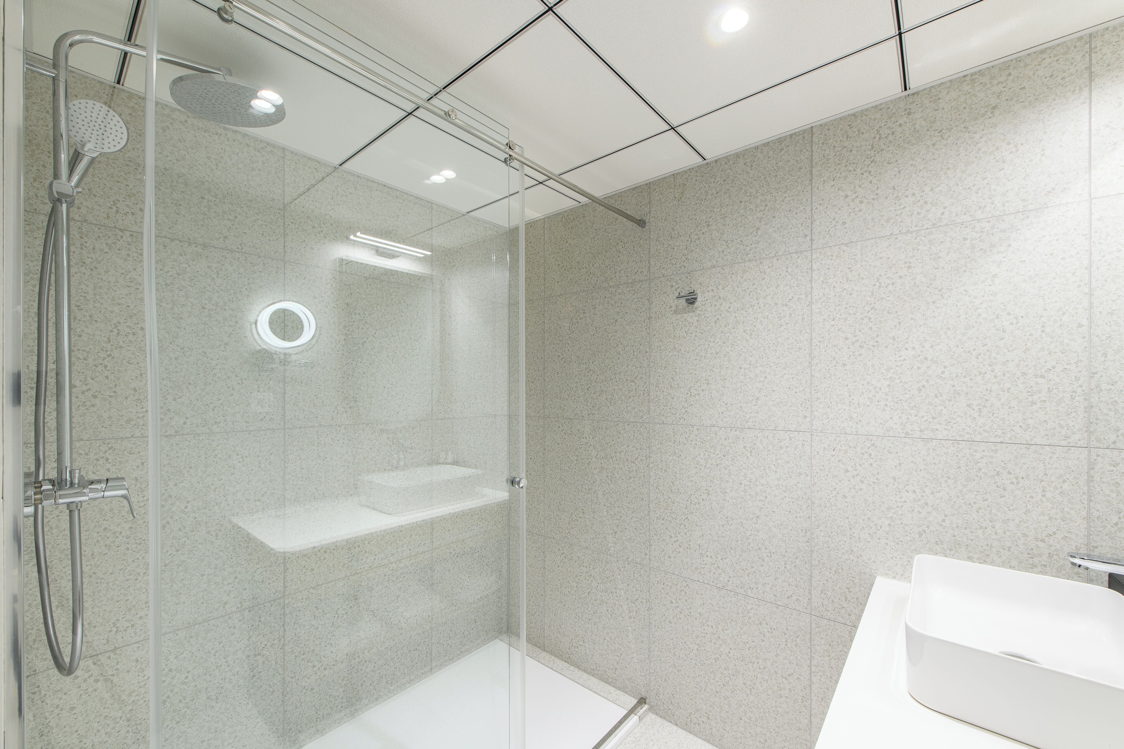 A modern bathroom with a glass-enclosed shower, a white sink, and a tiled floor.