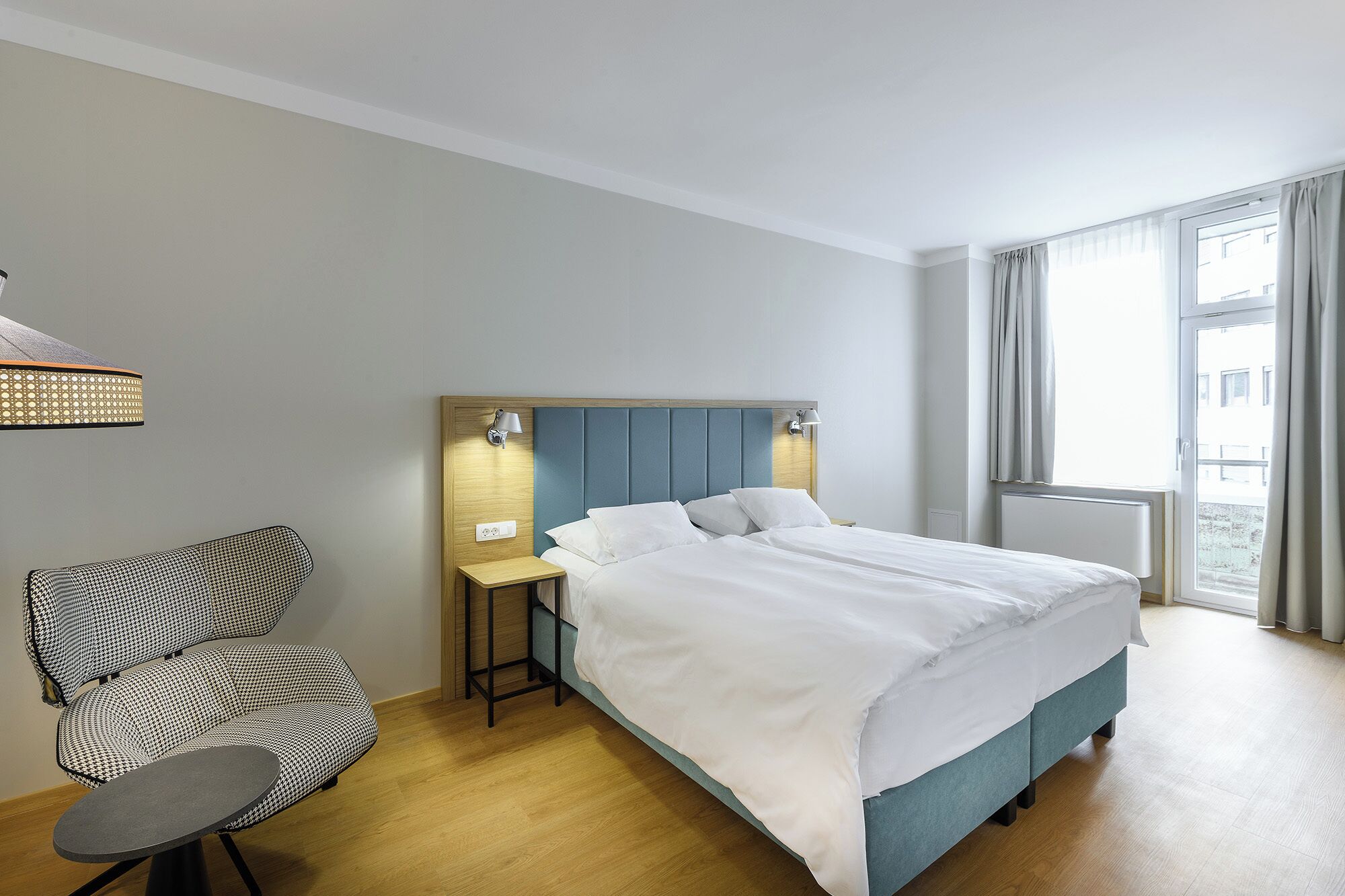 Et hotelværelse med seng, stol, natbord, lampe og et vindue med gardiner.