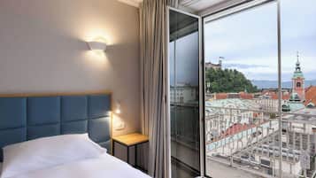 Une chambre d’hôtel avec une grande fenêtre, un lit, une table de chevet et une lampe fixée au mur.