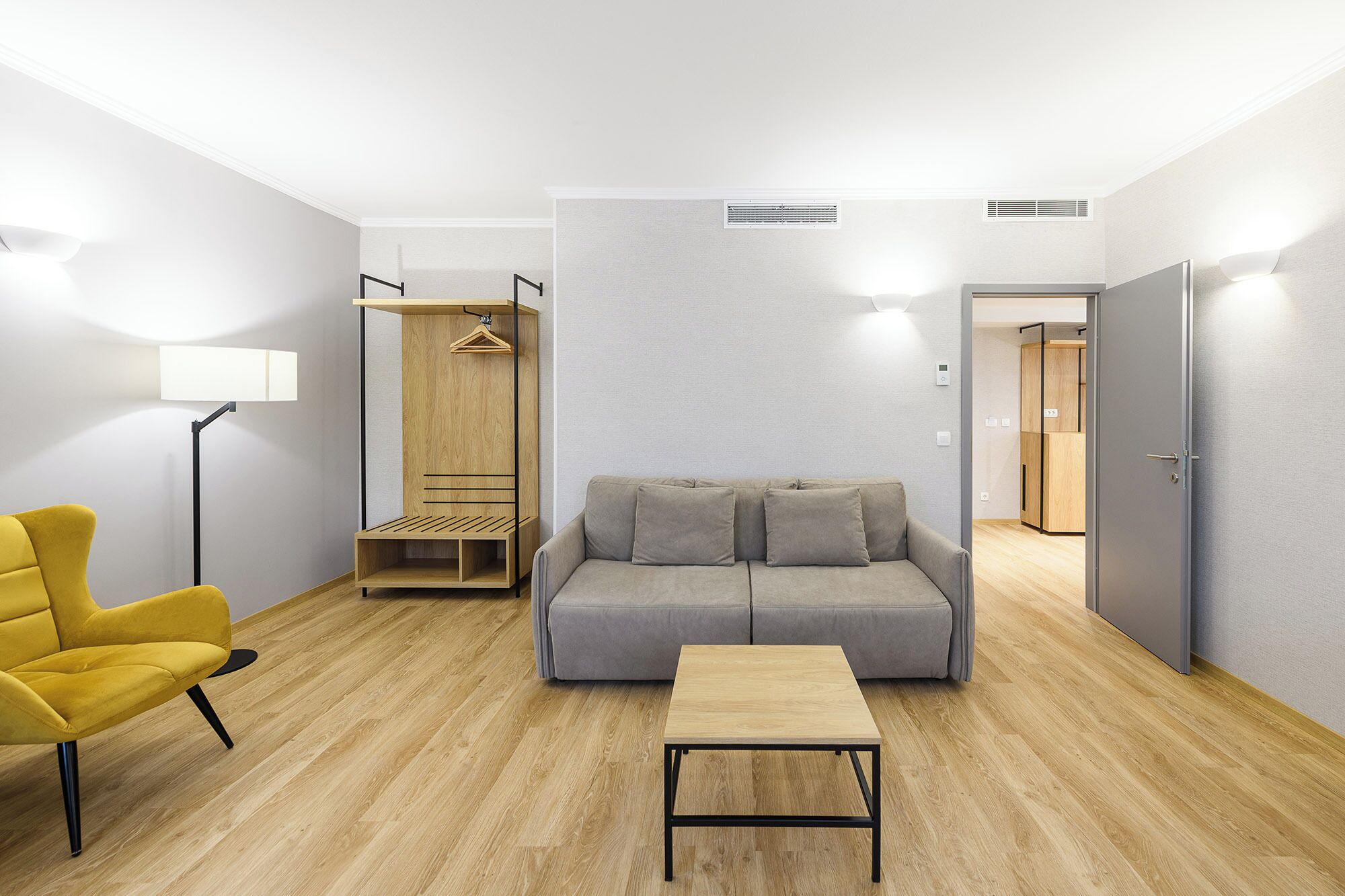 A modern living room with a sofa, a coffee table, a yellow armchair, a wooden wardrobe, and a floor lamp.