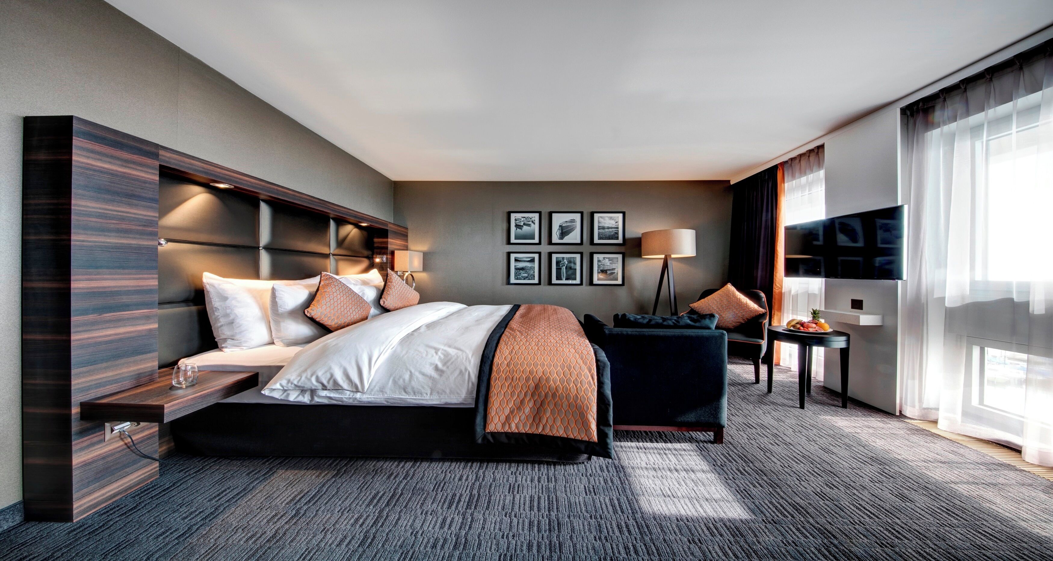 A modern hotel room with a large bed, a desk, a chair, a TV, and a window with curtains.