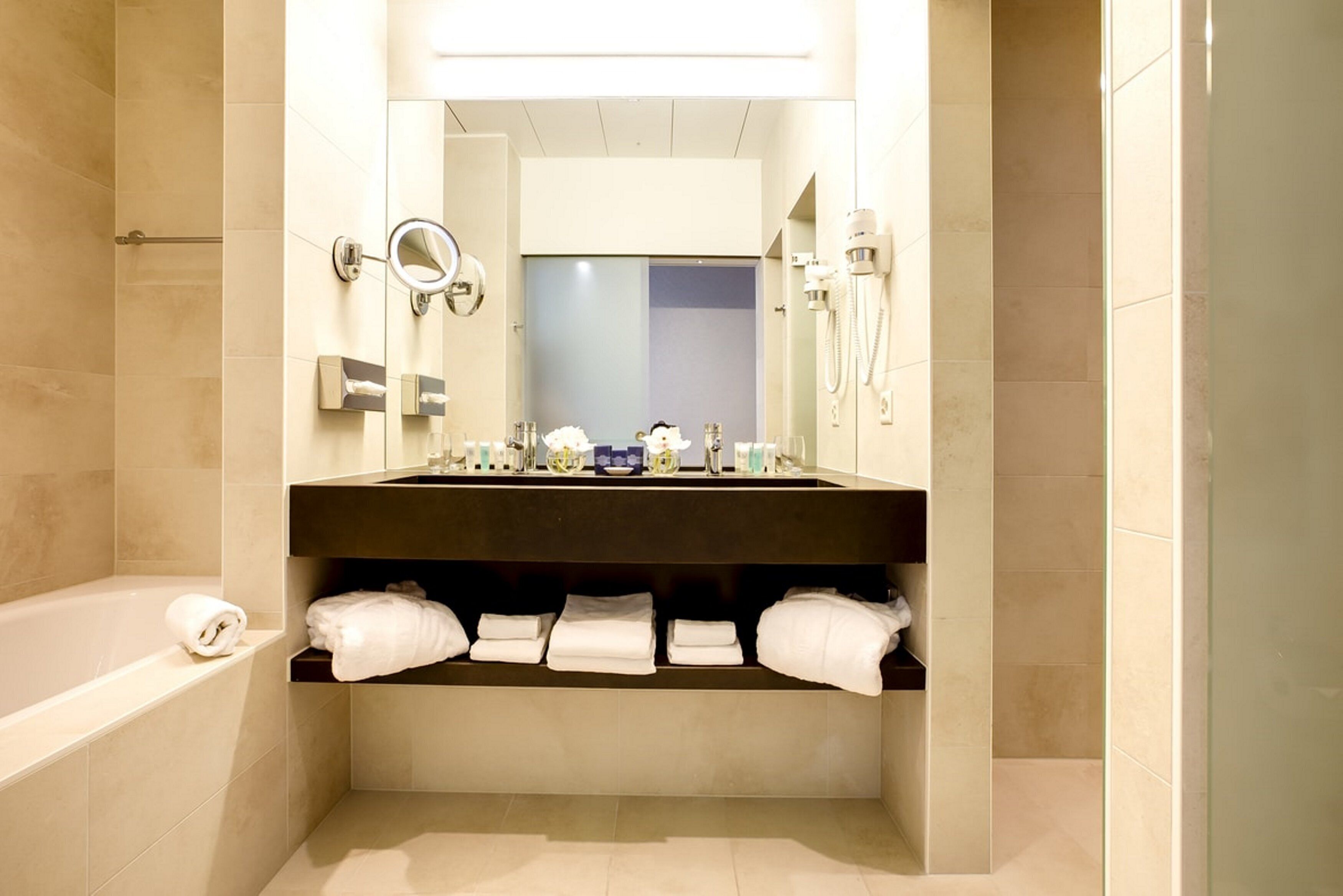 A modern bathroom with a large mirror, a bathtub, and a vanity with towels.