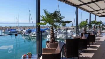 A marina with boats docked, a palm tree, and outdoor seating with a view of the sea.