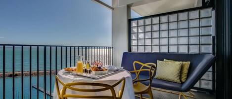 A balcony with a table set for breakfast, a sofa, and a view of the sea.