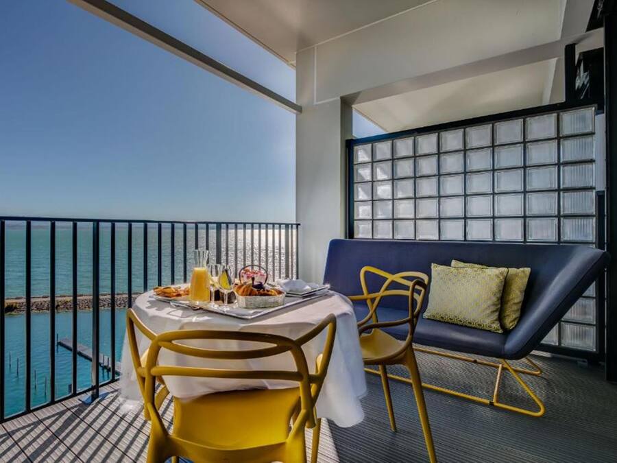 En balkong med ett bord dukat för frukost, en soffa och utsikt över havet.