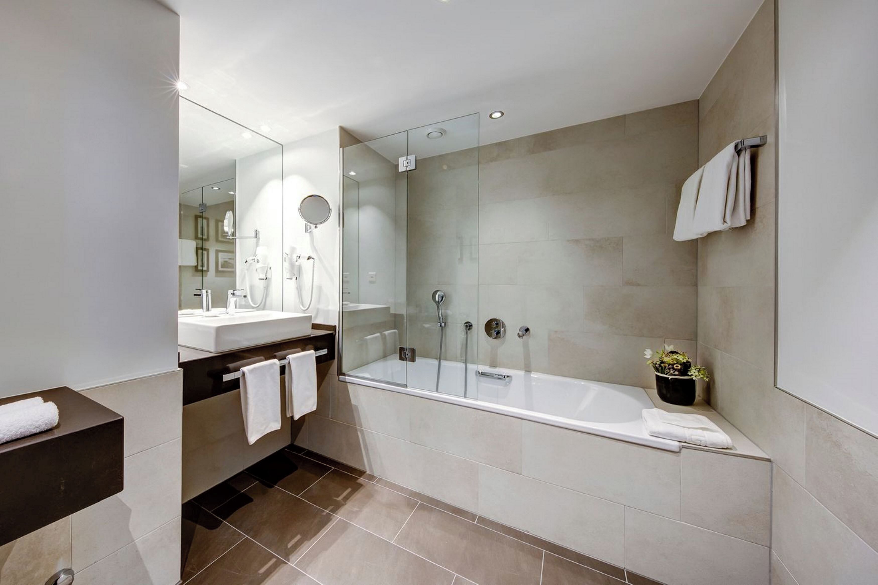 Een moderne badkamer met een douche met glazen wand, een ruim bad en een wastafel met spiegel.
