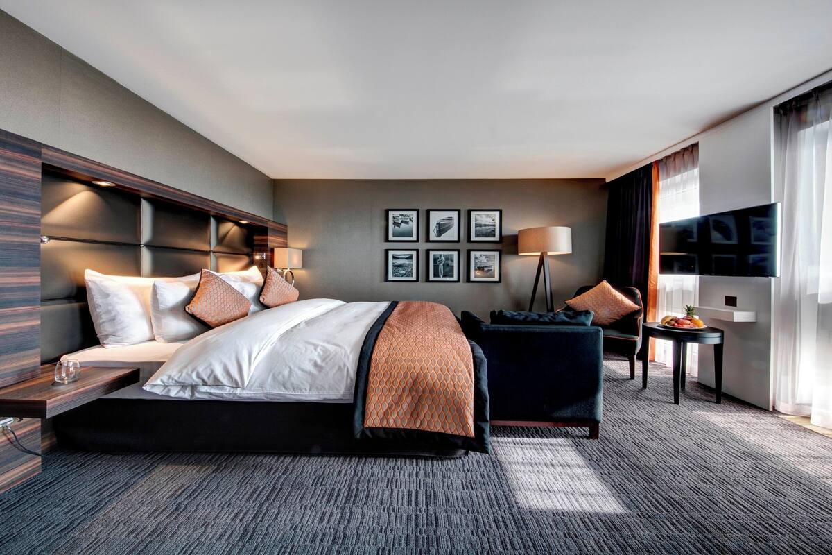 A modern hotel room with a large bed, a desk, a chair, a TV, and a window with curtains.