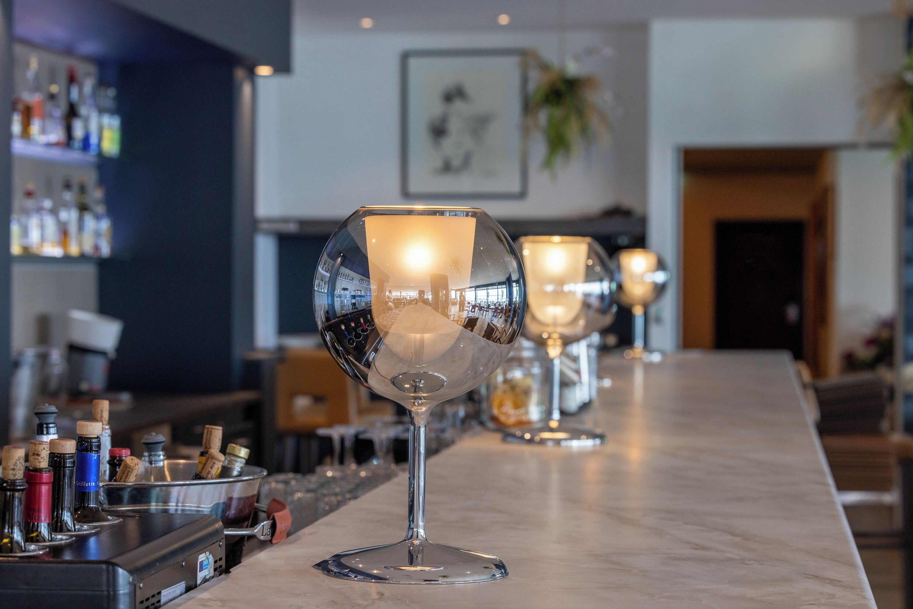 A bar area with wine glasses and bottles on the counter.