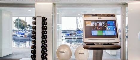 Un interior moderno con un quiosco digital, una fila de botellas negras y dos objetos esféricos con la etiqueta 'TECHNOGYM'.
