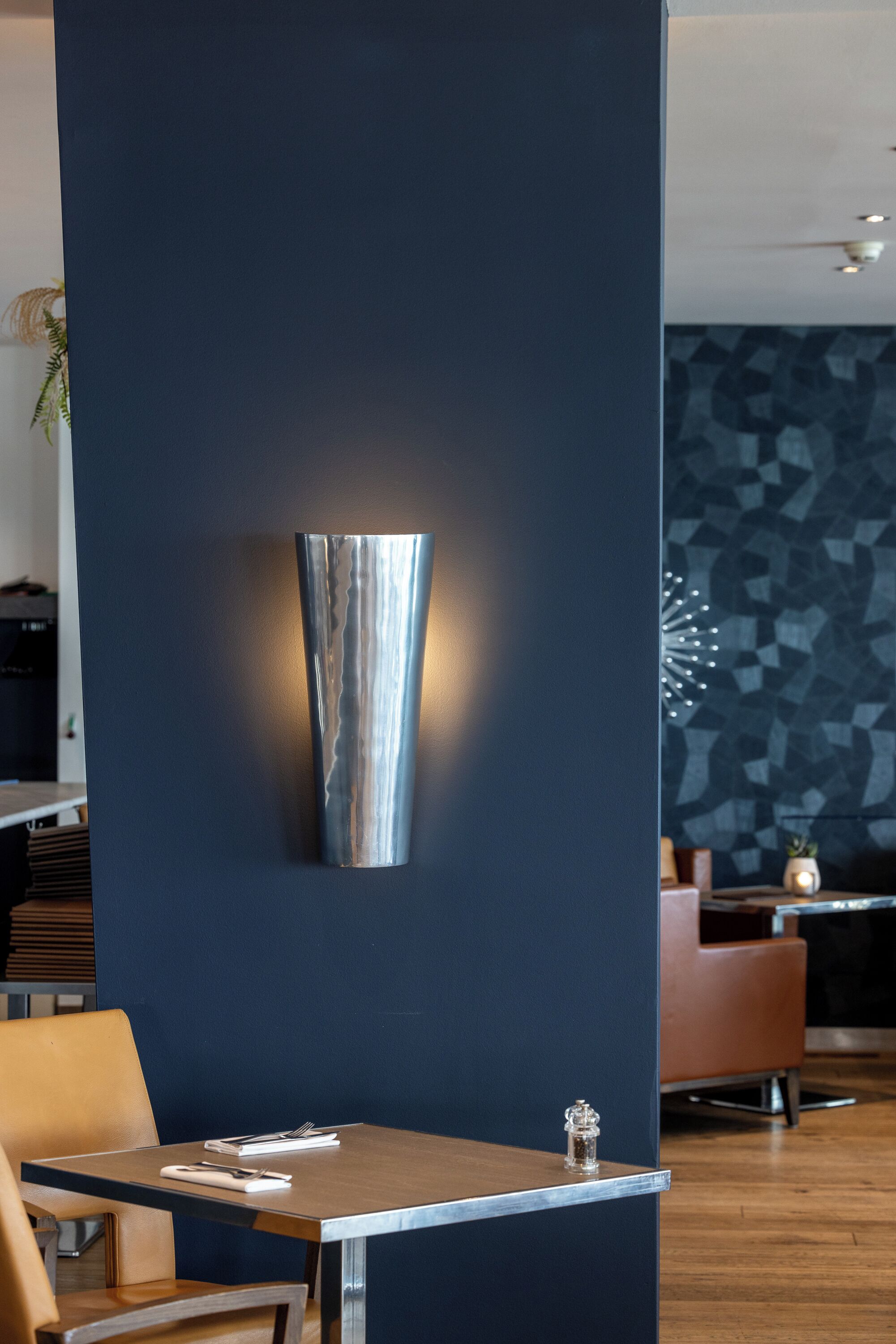 Un interior moderno con una pared azul oscuro, una lámpara metálica y una mesa de madera con una silla.