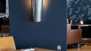 Un interior moderno con una pared azul oscuro, una lámpara metálica y una mesa de madera con una silla.