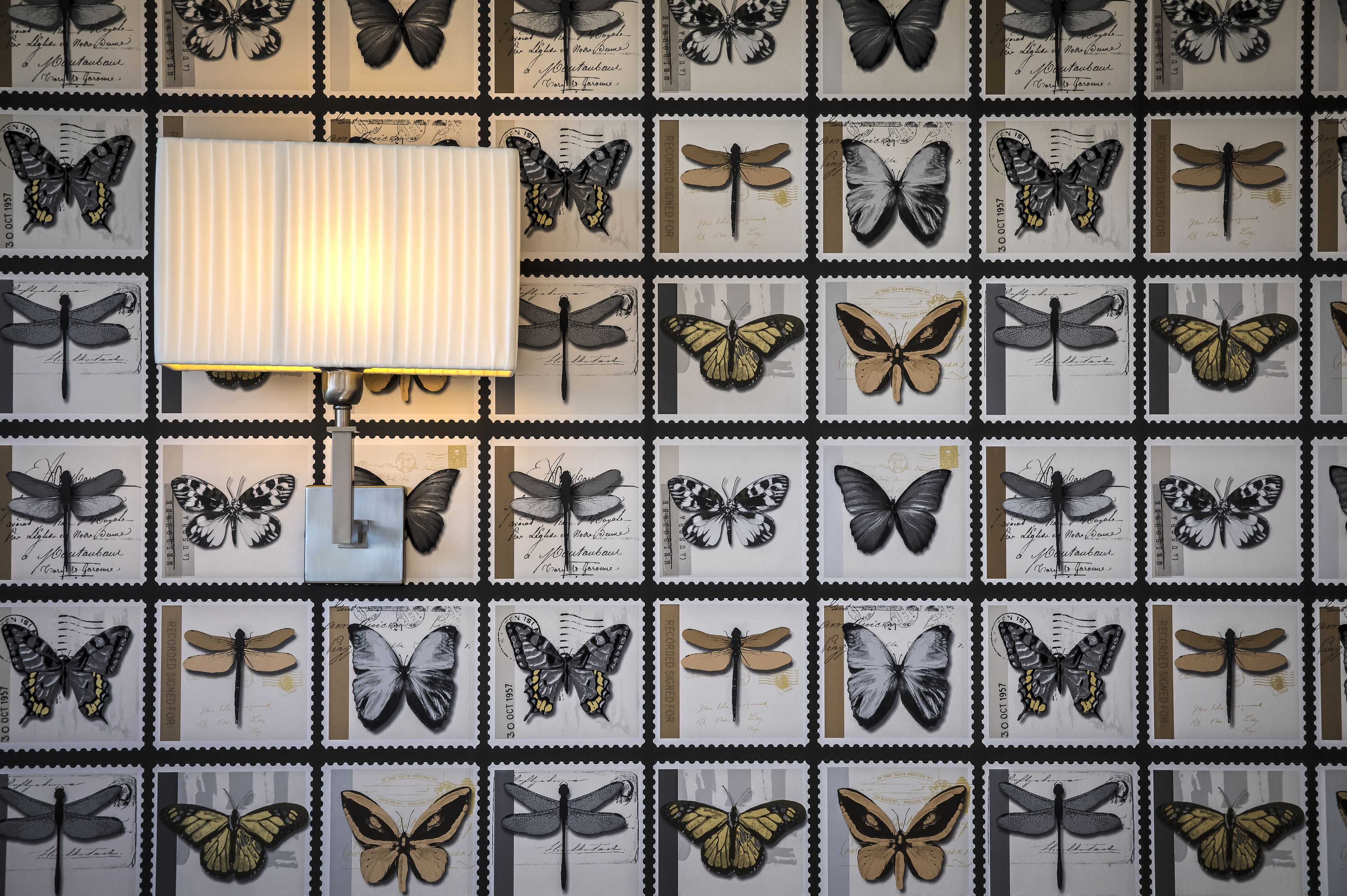A wall with a grid of butterfly illustrations, a lamp, and some text.