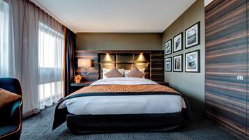 A hotel room with a large bed, a bedside table with a lamp, a chair, and a view of the city through the window.