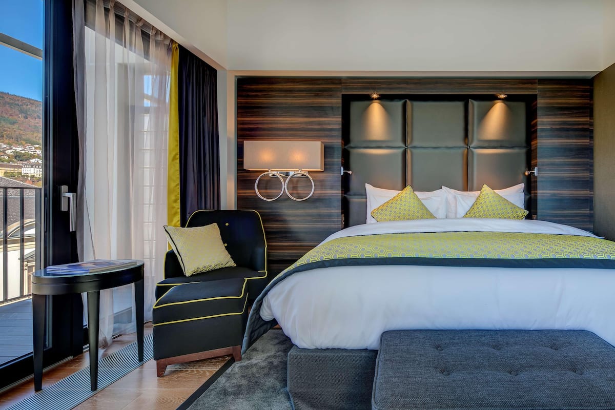 Habitación de hotel moderna con una cama grande, una mesita de noche, una silla y vistas al exterior.