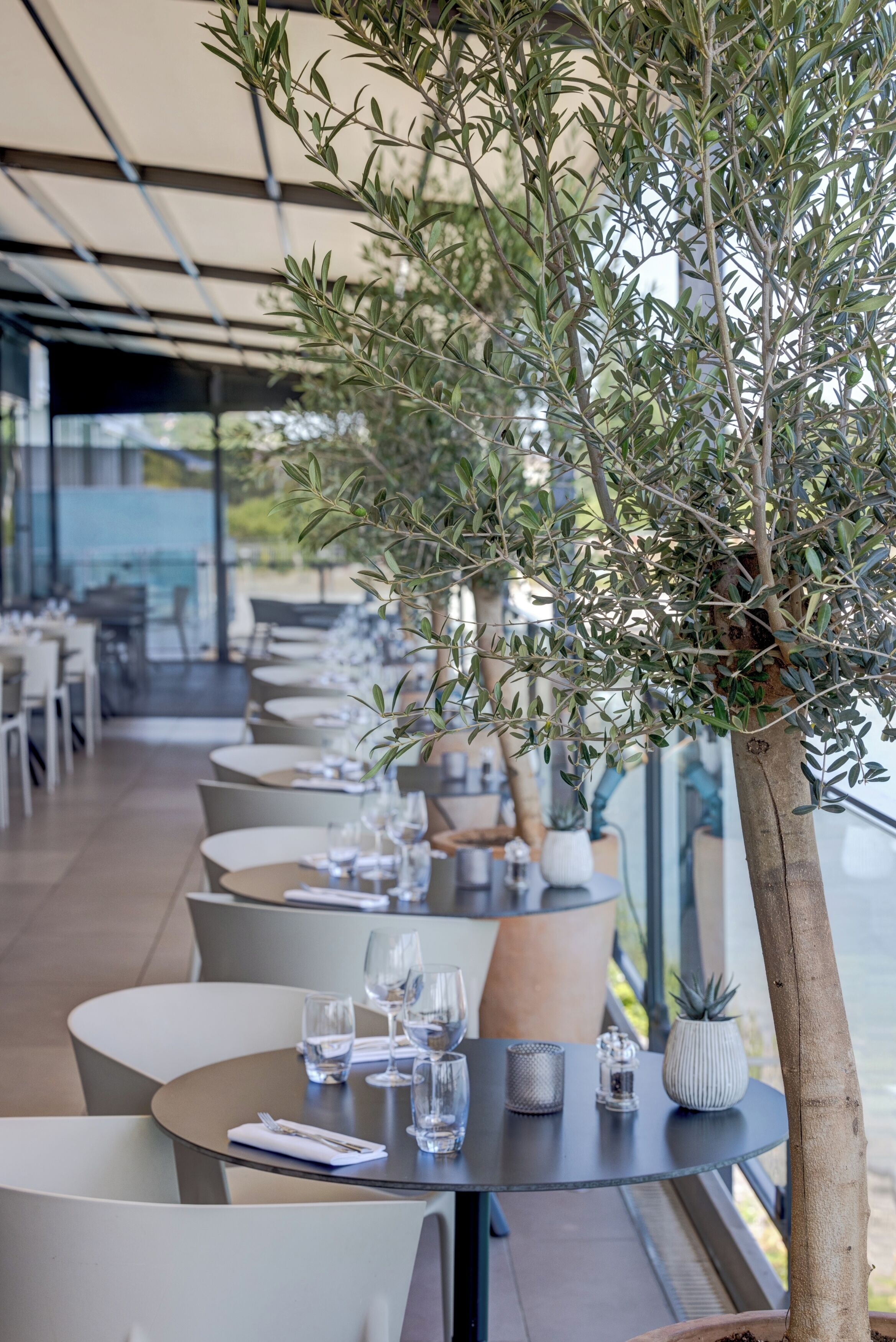 A row of tables with chairs, each set with a glass, cutlery, and a small decorative item.