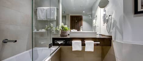 A modern bathroom with a glass shower enclosure, a bathtub, a vanity with a mirror, and a potted plant.