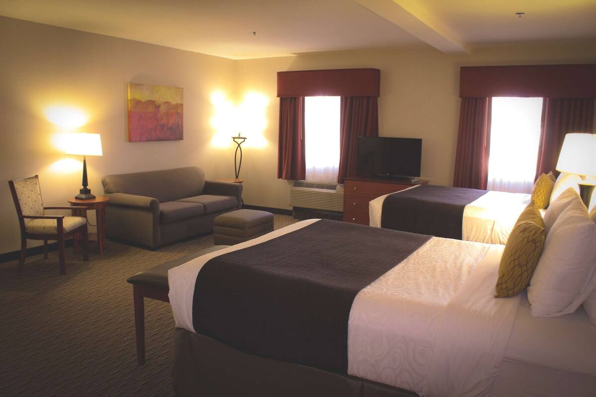 A hotel room with two beds, a TV, a desk, a chair, and a lamp.
