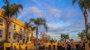 A pool area with lounge chairs, palm trees, and a building with a yellow facade.