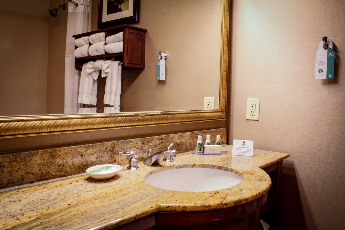 A bathroom with a granite countertop, a sink, a mirror, and a towel rack with folded towels.