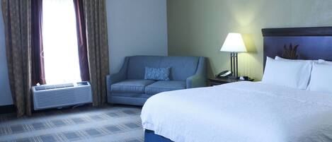 A hotel room with a bed, a sofa, a lamp, and a window with curtains.