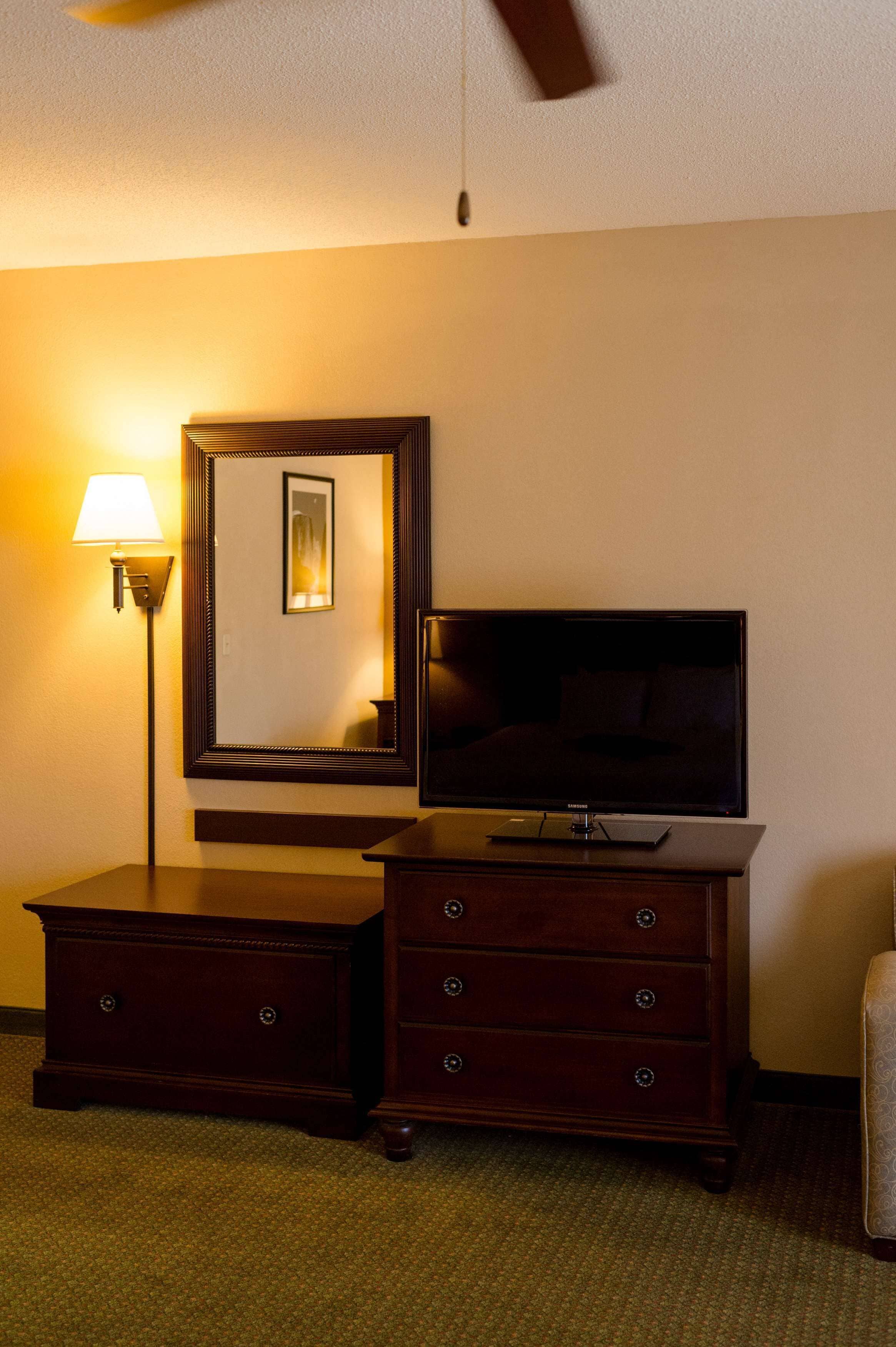 Habitación de hotel con televisor de pantalla plana sobre una cómoda de madera, una lámpara de pie y un ventilador de techo.
