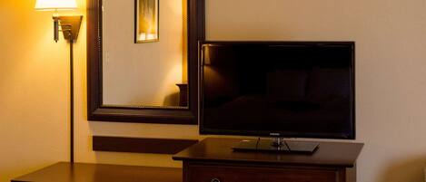 Habitación de hotel con televisor de pantalla plana sobre una cómoda de madera, una lámpara de pie y un ventilador de techo.